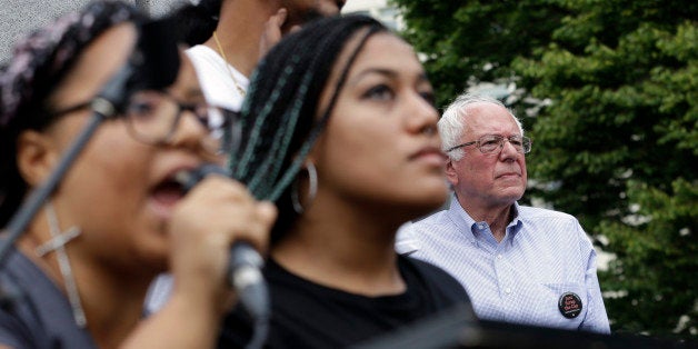 Marissa Johnson, left, speaks as Mara Jacqueline Willaford stands with her and Democratic presidential candidate Sen. Bernie Sanders, I-Vt., stands nearby as the two women take over the microphone at a rally Saturday, Aug. 8, 2015, in downtown Seattle. The women, co-founders of the Seattle chapter of Black Lives Matter, took over the microphone moments after Sanders began speaking and refused to relinquish it. Sanders eventually left the stage without speaking further and instead waded into the crowd to greet supporters. (AP Photo/Elaine Thompson)