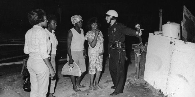 A policeman guides a group of women to safety during rioting in the Watts area of Los Angeles, August 1965. Their homes have