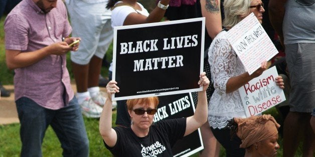 A woman holds a 'Black Lives Matter' sign during a memorial service for slain 18 year-old Michael Brown Jr. on August 9, 2015 at the Canfield Apartments in Ferguson, Missouri. Several hundred demonstrators stood in silence Sunday at the spot where an unarmed black teen was shot and killed by a white police officer one year ago, throwing America's troubled race relations into harsh relief. Two white doves were released over the crowd that gathered to mark the anniversary of 18-year-old Michael Brown's death in a fateful encounter August 9, 2014 with white police officer Darren Wilson. The crowd, about 300 strong, observed four and a half minutes of silence, one minute for each of the four and a half hours that Brown's body lay face down in the street before being taken away. AFP PHOTO / MICHAEL B. THOMAS (Photo credit should read Michael B. Thomas/AFP/Getty Images)