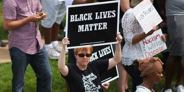 A woman holds a 'Black Lives Matter' sign during a memorial service for slain 18 year-old Michael Brown Jr. on August 9, 2015 at the Canfield Apartments in Ferguson, Missouri. Several hundred demonstrators stood in silence Sunday at the spot where an unarmed black teen was shot and killed by a white police officer one year ago, throwing America's troubled race relations into harsh relief. Two white doves were released over the crowd that gathered to mark the anniversary of 18-year-old Michael Brown's death in a fateful encounter August 9, 2014 with white police officer Darren Wilson. The crowd, about 300 strong, observed four and a half minutes of silence, one minute for each of the four and a half hours that Brown's body lay face down in the street before being taken away. AFP PHOTO / MICHAEL B. THOMAS (Photo credit should read Michael B. Thomas/AFP/Getty Images)
