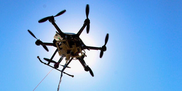 A water collecting drone with it's three containers and collection tube is silhouetted by the sun at a testing site in Lincoln, Neb., Friday, Sept. 6, 2013. A team led by Nebraska university scientists has won a federal grant to further develop aerial drones that could hover over and sample water from lakes, ponds and streams that people can't easily reach. The team have already developed a drone that can collect and carry three samples. They'll use the USDA money to perfect algorithms to improve its safety and reliability. The drone is tethered by a pink rope per FAA rules. (AP Photo/Nati Harnik)