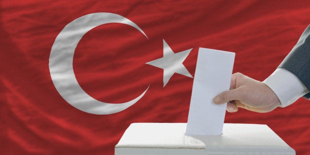 man putting ballot in a box during elections in turkey in front of flag