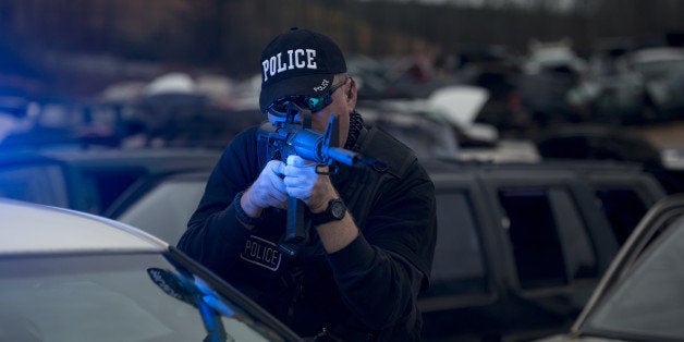 A police officer and police vehicle with a Bushmaster rifle in response situation.