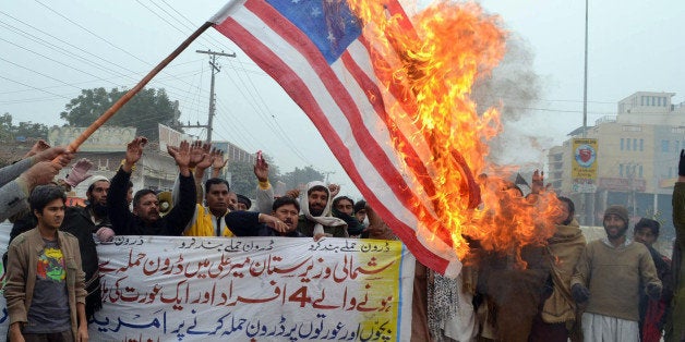 Pakistani demonstrators shout slogans beside a burning US flag during a protest in Multan on January 3, 2013, against the dro
