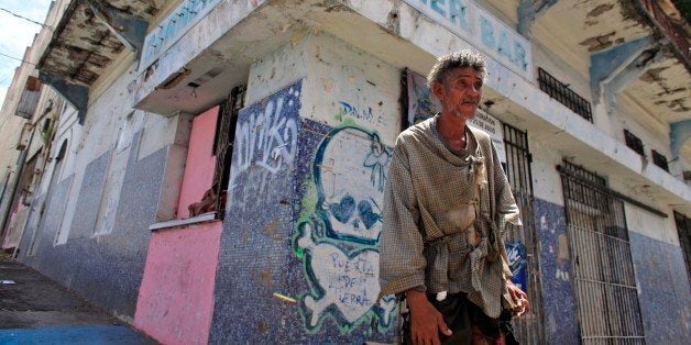 A homeless man stands in front of a closed down business in Puerta de Tierra in the outskirts of Old San Juan, Puerto Rico, Sunday, Aug. 2, 2015. Mired in a 10 year old economic crisis, Puerto Rico failed to pay a $58 million bond payment due Saturday. If defaults continue, analysts say Puerto Rico will face numerous lawsuits and increasingly limited access to markets, putting a recovery even more out of reach. (AP Photo/Ricardo Arduengo)