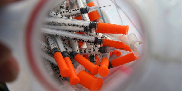 In this Thursday, Oct. 29, 2015 photograph, a jug of used needles to exchange for new is seen near, Jim "Woods" Ellis in an industrial area of Camden, N.J., as Ellis describes using the drug, naloxone, often known by the brand name Nacran, to reverse an addict's heroin overdose. Naloxone works most of the time, but national statistics arenât kept on what happens to people who are revived. Some overdose again soon afterward. Some get treatment and get clean, but limited insurance, high costs and a shortage of spots at treatment centers can be hurdles. (AP Photo/Mel Evans)