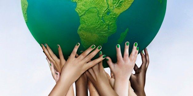 Multiracial hands holding green globe against sky background 