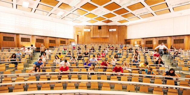Group of college students in the university amphitheatre, they are sitting and doing an exam. Two professors are monitoring t
