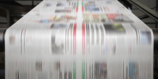 A large offset printing press running a long roll off paper over its rollers at high speed.