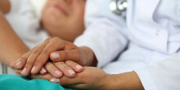 Friendly female doctor's hands holding patient's hand lying in bed for encouragement, empathy, cheering and support while medical examination. Trust and ethics concept. Bad news lessening and support