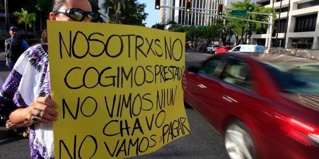 A protestor holds a sign that reads in Spanish: "We didn't take out a loan. We didn't see a dime. We're not going to pay." during a protest in the financial district demanding the island's public debt not be paid to bondholders in San Juan, Puerto Rico, Wednesday, July 15, 2015. Protesters gathered at what is known as The Golden Mile to demand the banking industry take responsibility for the current economic crisis. This month Gov. Alejandro Garcia Padilla said Puerto Rico's outstanding $72 billion public debt is unpayable given the island's long recession. (AP Photo/Ricardo Arduengo)