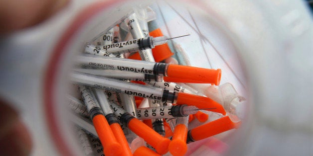 In this Thursday, Oct. 29, 2015 photograph, a jug of used needles to exchange for new is seen near, Jim "Woods" Ellis in an