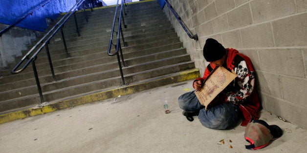 A homeless man holds a sign asking for money while resting at the entrance to a subway station, Friday, Oct. 9, 2015 in New York. (AP Photo/Mark Lennihan)