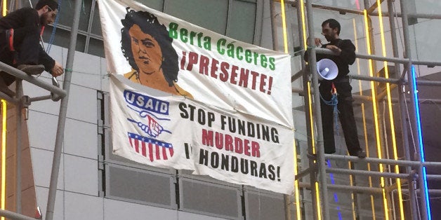 Two men hold two banners which read âBerta Cáceres Presente!â and âUSAID STOP FUNDING MURDER HONDURASâ in the atrium of the Ronald Reagan building in Washington, on Monday March 14 2016. Berta Caceres was a Honduran activist who was killed earlier this month in her house. (AP Photo/Luis Alonso Lugo)