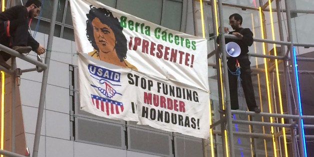 Two men hold two banners which read âBerta CÃ¡ceres Presente!â and âUSAID STOP FUNDING MURDER HONDURASâ in the atrium of the Ronald Reagan building in Washington, on Monday March 14 2016. Berta Caceres was a Honduran activist who was killed earlier this month in her house. (AP Photo/Luis Alonso Lugo)