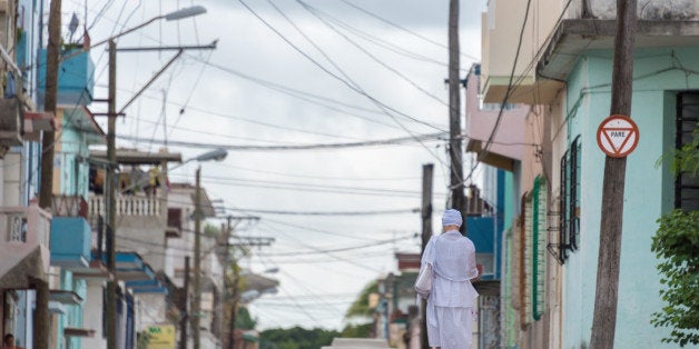 HAVANA, CUBA - 2015/09/19: Afro religious woman with crisscrossing overhead electric wires and a woman dressed in traditional clothes walking on the street. (Photo by Roberto Machado Noa/LightRocket via Getty Images)