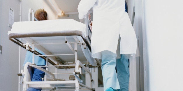 Rear View of Doctors in Surgical Scrubs Hurrying Down a Hospital Corridor With a Trolley