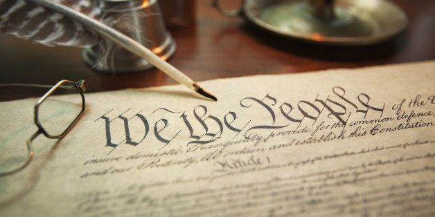 Selective focus image of the United States Constitution with quill pen, glasses and candle holder