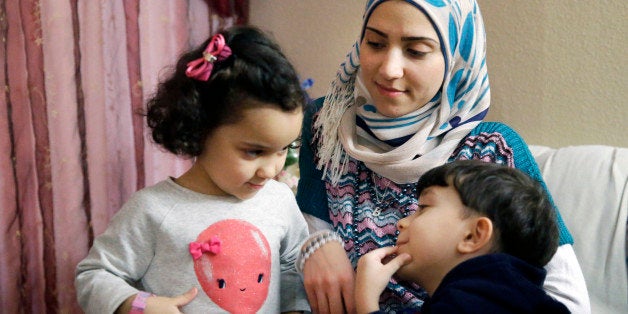 In this photo made Monday, Nov. 29, 2015, Syrian refugee Maryam al Jaddou, center, looks on as her children twins Maria, left, and Hasan, sit with her at their apartment in Dallas. The 30-year-old al Bashar al Jaddou decided to leave Syria in 2012 after his familyâs home in Homs was bombed and there was nowhere safe left to live. (AP Photo/LM Otero)