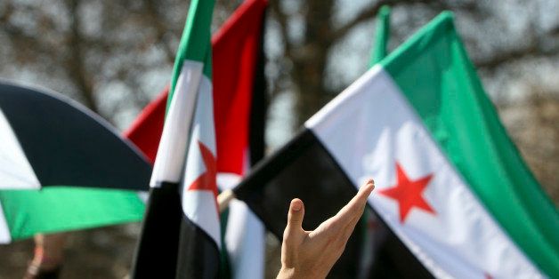 Human hand waving in front of Syrian flags.