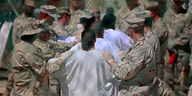 In this photo, reviewed by the U.S. military, guards stand on either side of a line-up of Guantanamo detainees, in white, to perform a search for unauthorized items, at Guantanamo's Camp 4 detention facility, at Guantanamo Bay U.S. Naval Base, Cuba, Tuesday, May 12, 2009. (AP Photo/Brennan Linsley)