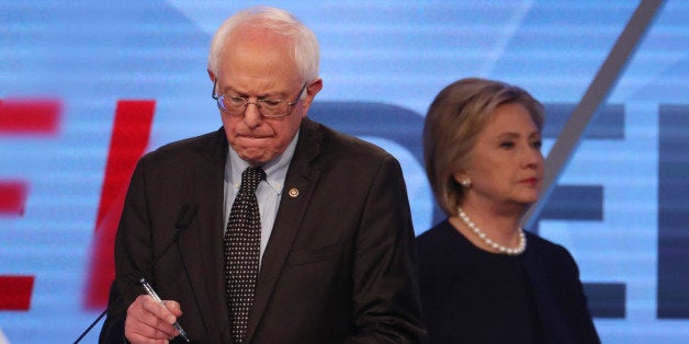 Democratic U.S. presidential candidate Senator Bernie Sanders writes on his notes as his rival Hillary Clinton walks behind him to her podium during a commercial break at the Univision News and Washington Post Democratic U.S. presidential candidates debate in Kendall, Florida March 9, 2016. REUTERS/Carlo Allegri