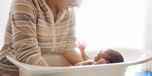 An asian woman bathing her baby in baby bathtub. They are looking each other.