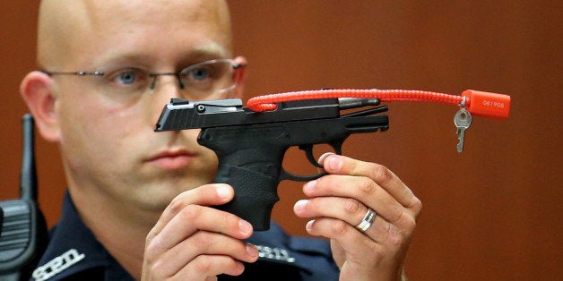 FILE- In this June 28, 2013, file photo, Sanford police officer Timothy Smith holds up the gun that was used to kill Trayvon