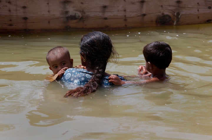 A woman displaced by flooding carries her children to a boat as they return to Bobak, Pakistan, in 2010. An Intergovernmental Panel on Climate Change report warns that “climate change will be a poverty-multiplier that makes poor people poorer.”