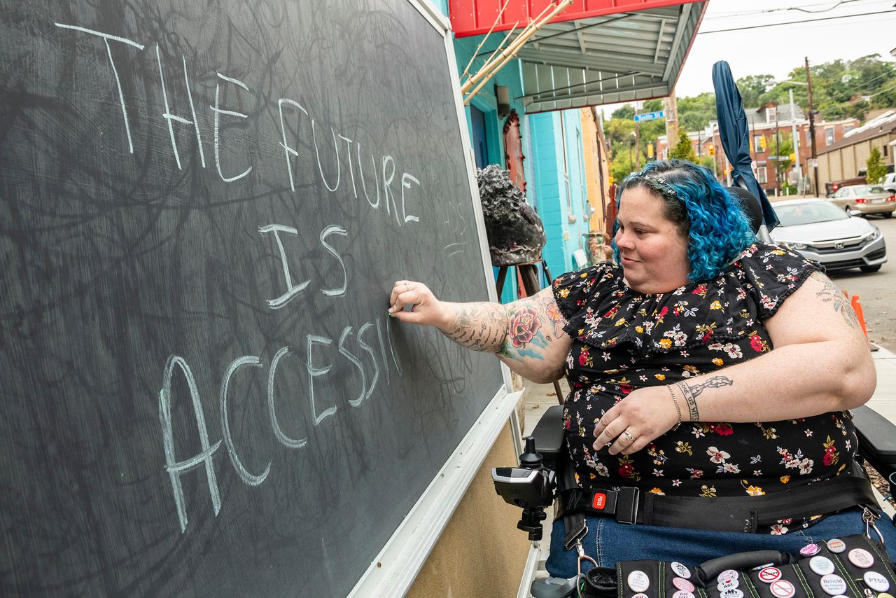 Alisa Grishman writes "The Future is Accessible" on a chalkboard of a neighborhood business.