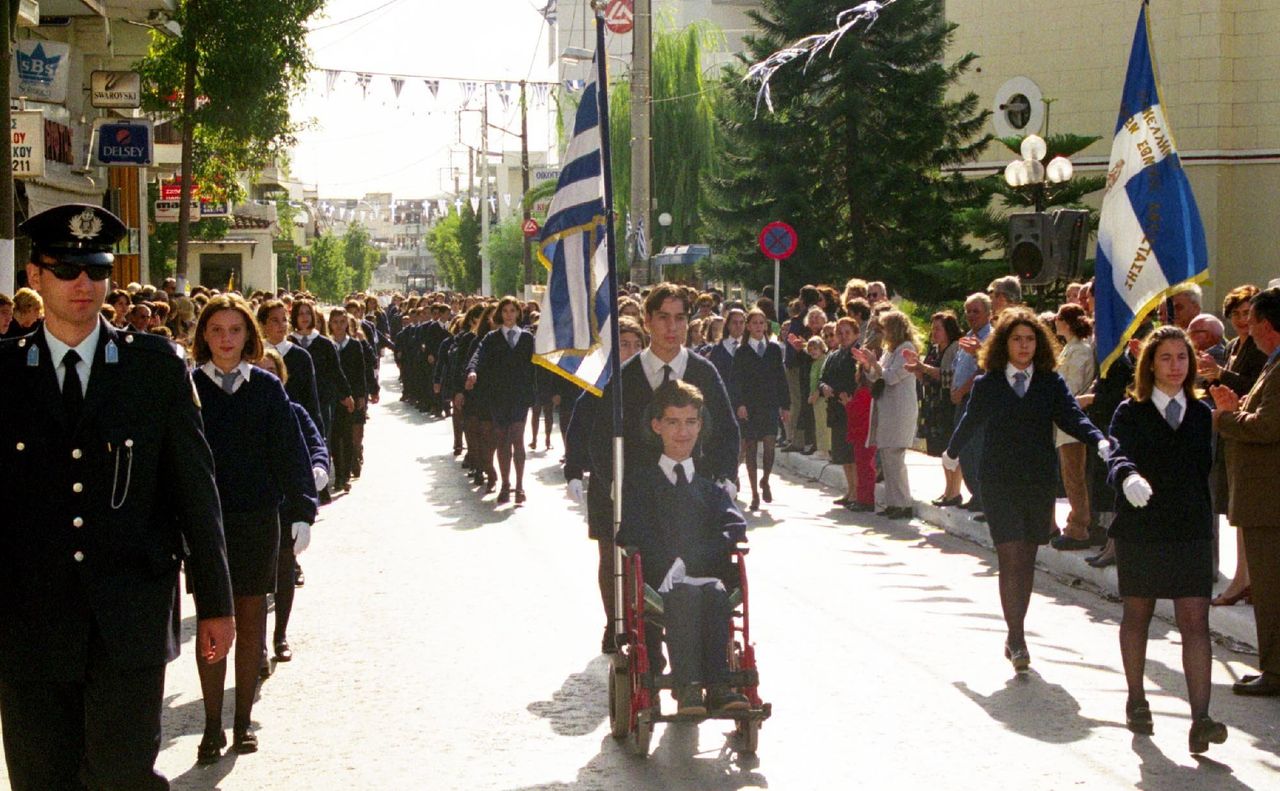 Ο Στέλιος Κυμπουρόπουλος, σε ηλικία 14 ετών, γίνεται ο πρώτος σημαιοφόρος μαθητής με κινητική αναπηρία. Κορωπί, 28 Οκτωβρίου 1999. 