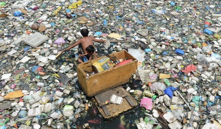 A father and son paddle through a garbage-filled river as they collect plastic bottles to sell in junk shops in Manila, Philippines.