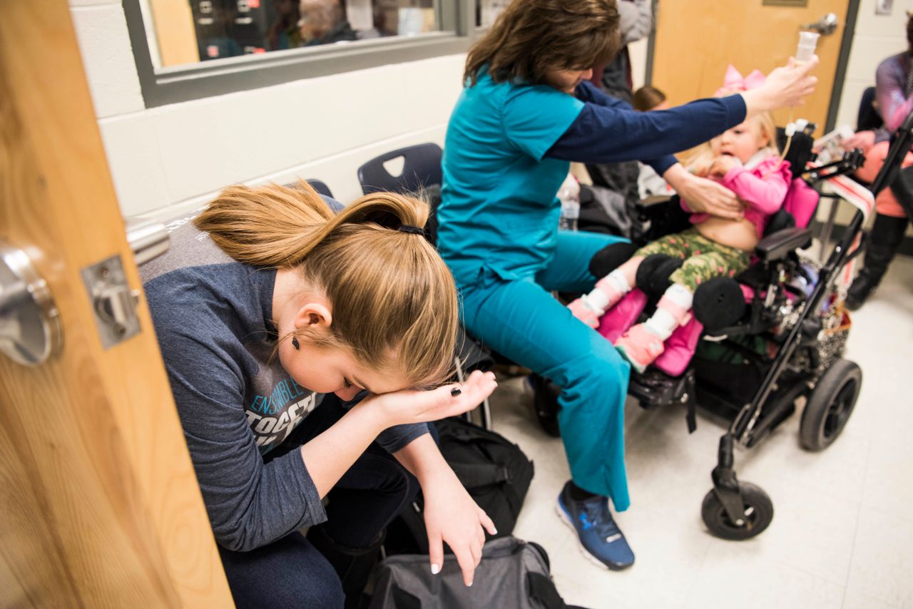 Kylee listens in the back of a classroom at her high school where her mother is giving a presentation about her sister's condition. Glenda is feeding Willow through a feeding tube.