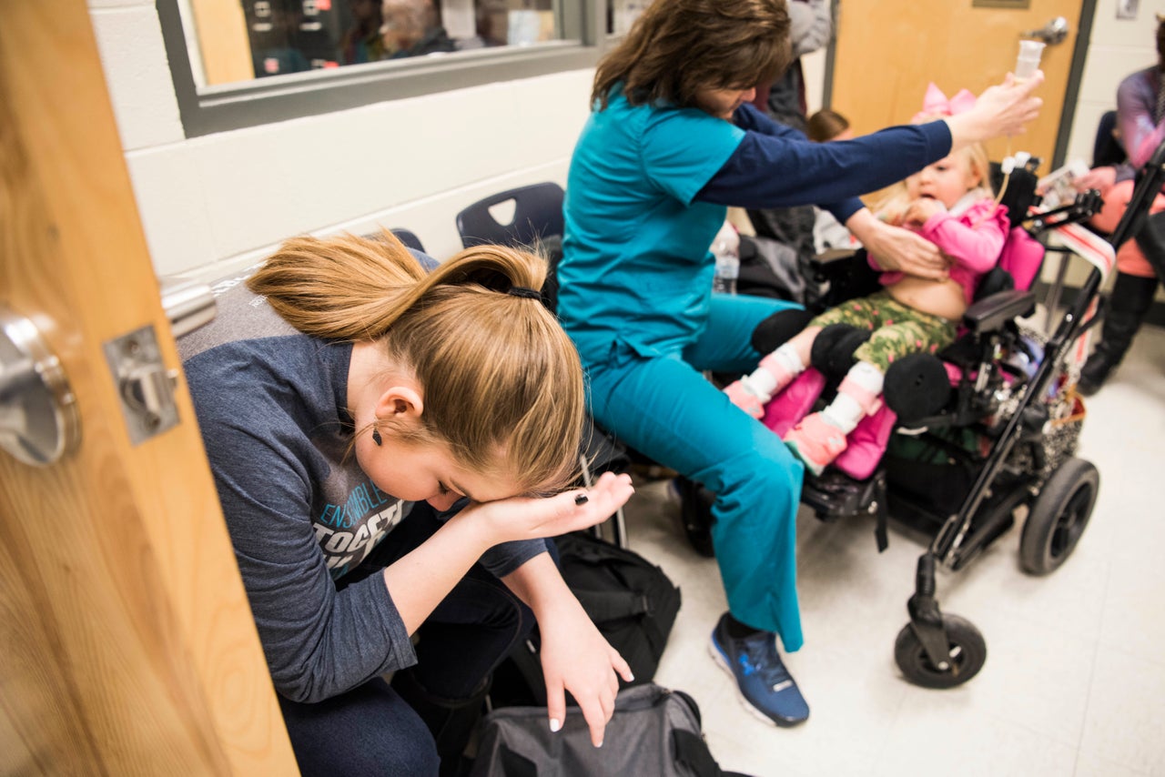 Kylee listens in the back of a classroom at her high school where her mother is giving a presentation about her sister's condition. Glenda is feeding Willow through a feeding tube.