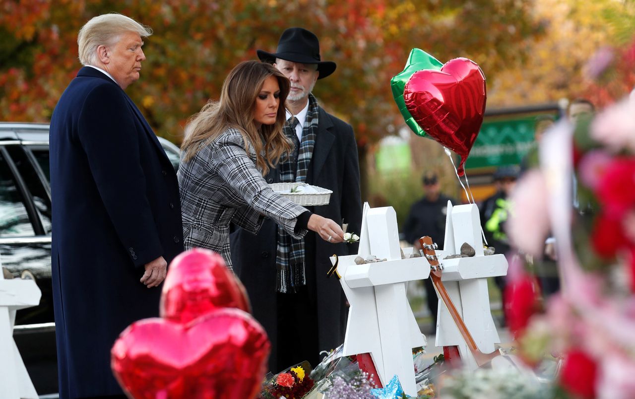President Donald Trump watches as first lady Melania Trump places a flower on a memorial to shooting victims as they stand with Tree of Life Synagogue Rabbi Jeffrey Myers.