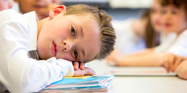 A close up shot of a little boy at school who looks distant and upset.