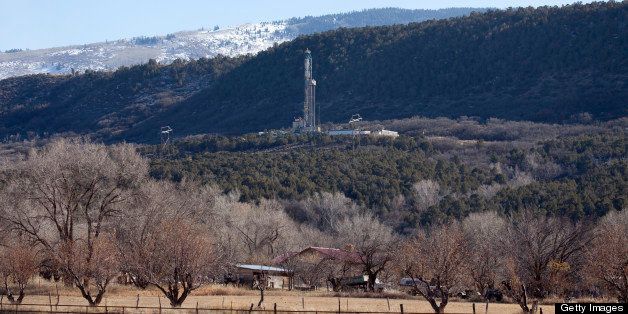 With the snow covered Rocky Mountains in the background, a home stands in front of a pine forest with a drilling rig (Colorado Nabors Rig #573) for natural gas near Rifle, Colorado.