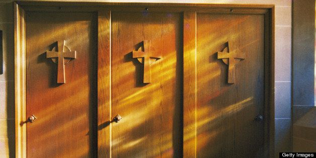 Confessional doors are bathed in soft sunlight shining through stained glass windows