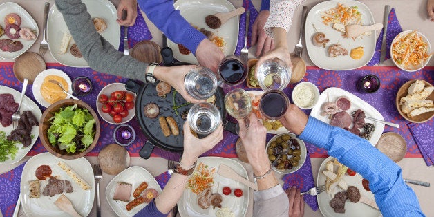 high angle view people toasting over dining table with seafood and meat to grill and on plates with various sauces and salads