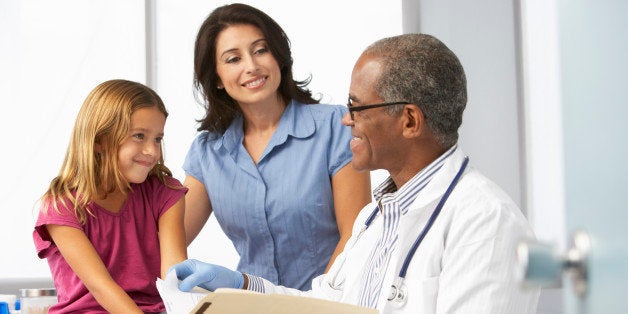 Smiling Doctor In Surgery Examining Young Girl With Mother.