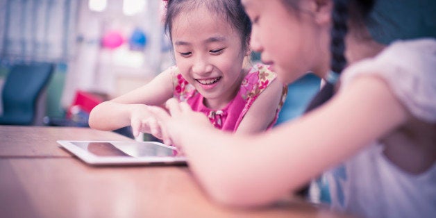 Two primary students using tablet in classroom.