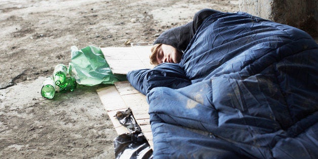 Homeless man sleeping in sleeping bag on cardboard