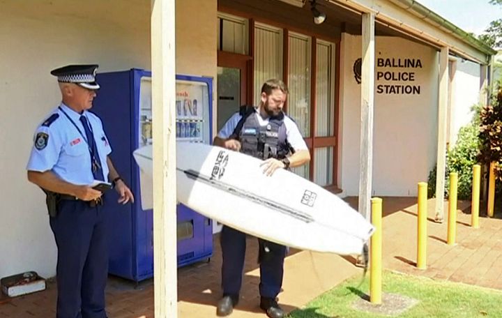 A police officer holds a victim's surfboard at a police station in Ballina, Australia