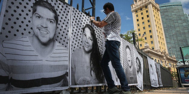 MIAMI, FL - AUGUST 31: Luis Gomez attaches pictures to a fence near the Freedom Tower as he helps hang the 'Inside Out 11M'