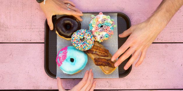 Three hands reaching in for an assortment of colorful doughnuts.