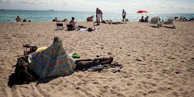 A homeless person lies in the sand in the South Beach neighborhood of Miami Beach, Florida, U.S., on Wednesday, Feb. 20, 2013. U.S. exports in the travel and tourism sector reached $168.1 billion in 2012, up 10.1 percent from the year-ago level of $152.7 billion, according to data released Feb. 22 by the Commerce Department's International Trade Administration. Photographer: Ty Wright/Bloomberg via Getty Images