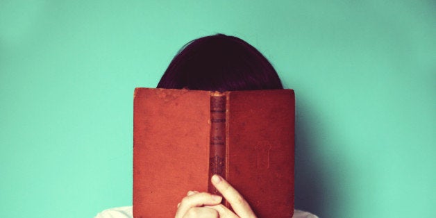 Woman's holding a book in front of her face.