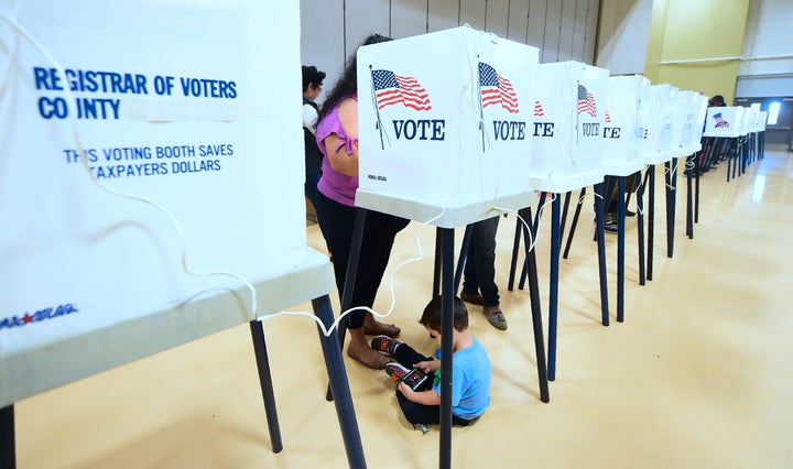 A woman votes from a booth as her child plays with a cellphone below inside the gymnasium at the Barack Obama Prep Academy on