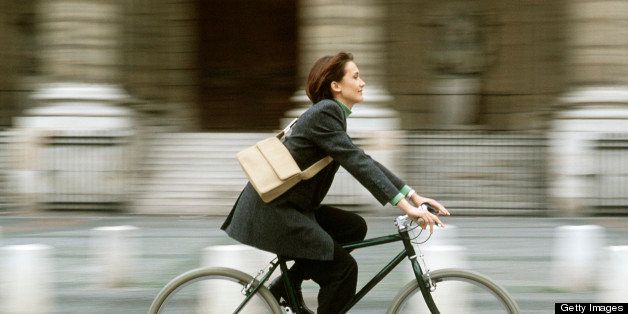 Well dressed woman riding bicycle down city sidewalk