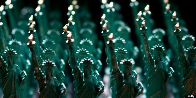 Rows of miniature green Statue of Liberty figurines, bearing golden flames.